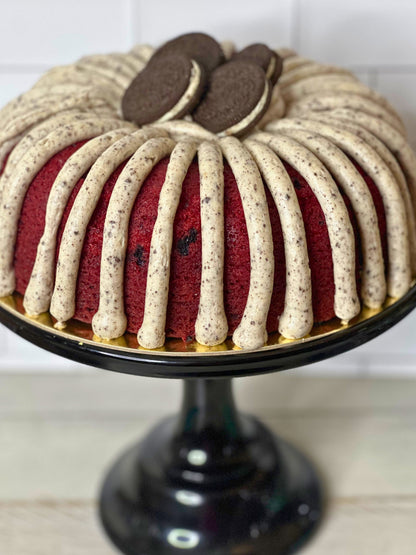 Red velvet bundt cake with cream cheese frosting on a black cake stand.